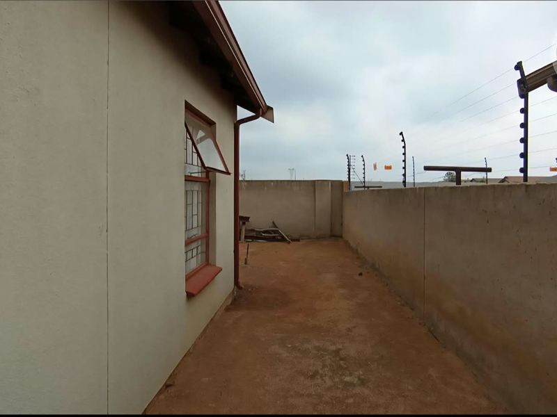 A side exterior area featuring a perimeter wall with electric fencing and a window with security bars.
