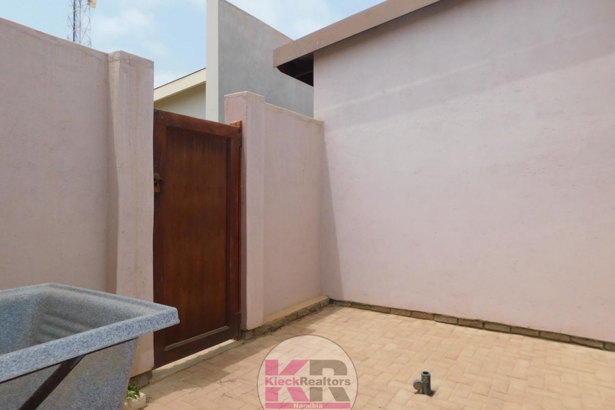A private outdoor courtyard area featuring paved flooring, a wooden access gate, and perimeter boundary walls.