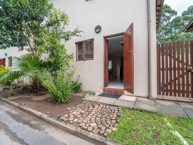 Front entrance of the townhouse featuring a timber door, cobblestone pathway, and surrounding garden area.