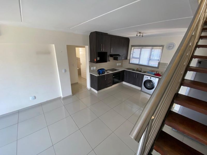 Open-plan kitchen area featuring dark wood cabinetry, integrated appliances, and tiled flooring, adjacent to a staircase leading to the upper level.