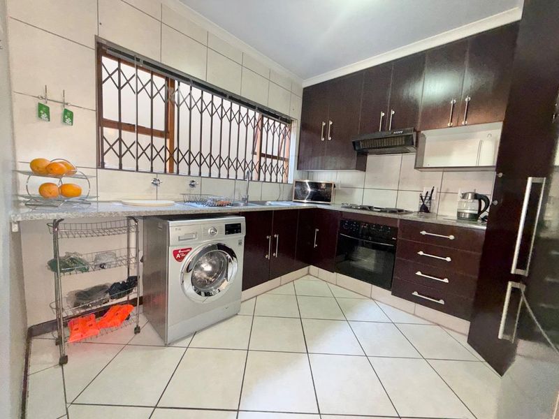 Functional kitchen featuring dark wood cabinetry, granite countertops, built-in oven with gas hob, and tiled flooring with integrated laundry plumbing.