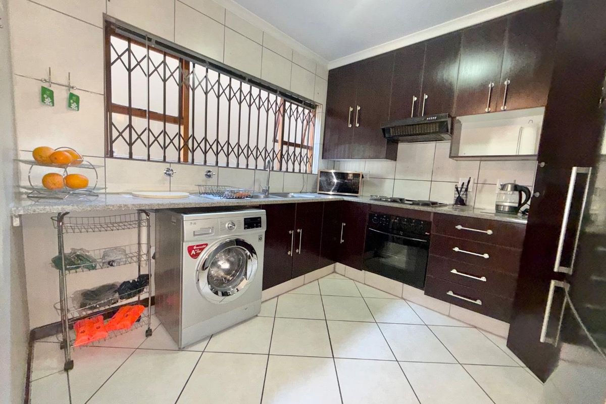 Functional kitchen featuring dark wood cabinetry, granite countertops, built-in oven with gas hob, and tiled flooring with integrated laundry plumbing.