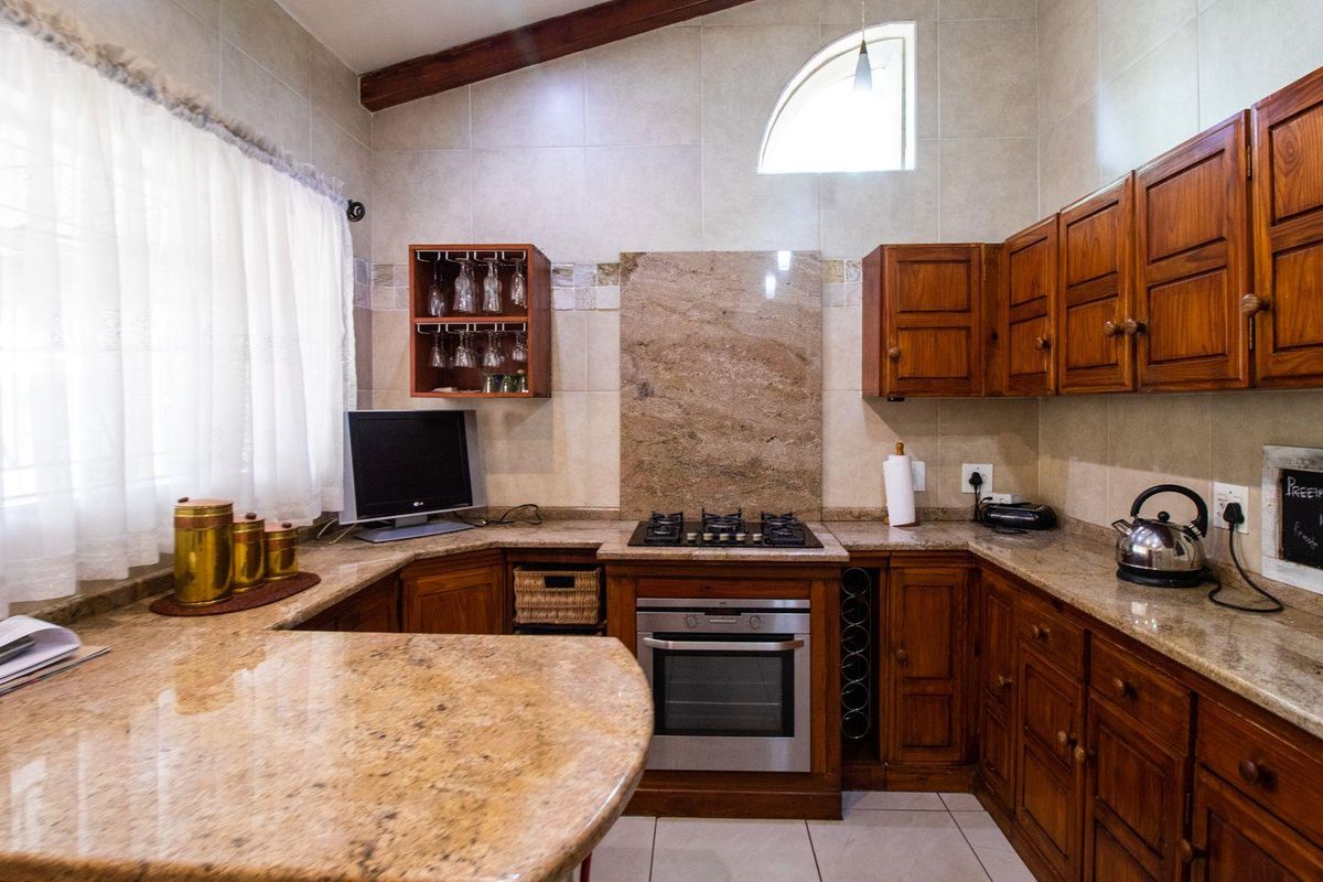 A functional kitchen featuring solid wood cabinetry, granite countertops, a built-in oven, gas hob, and a vaulted ceiling with a feature arched window.