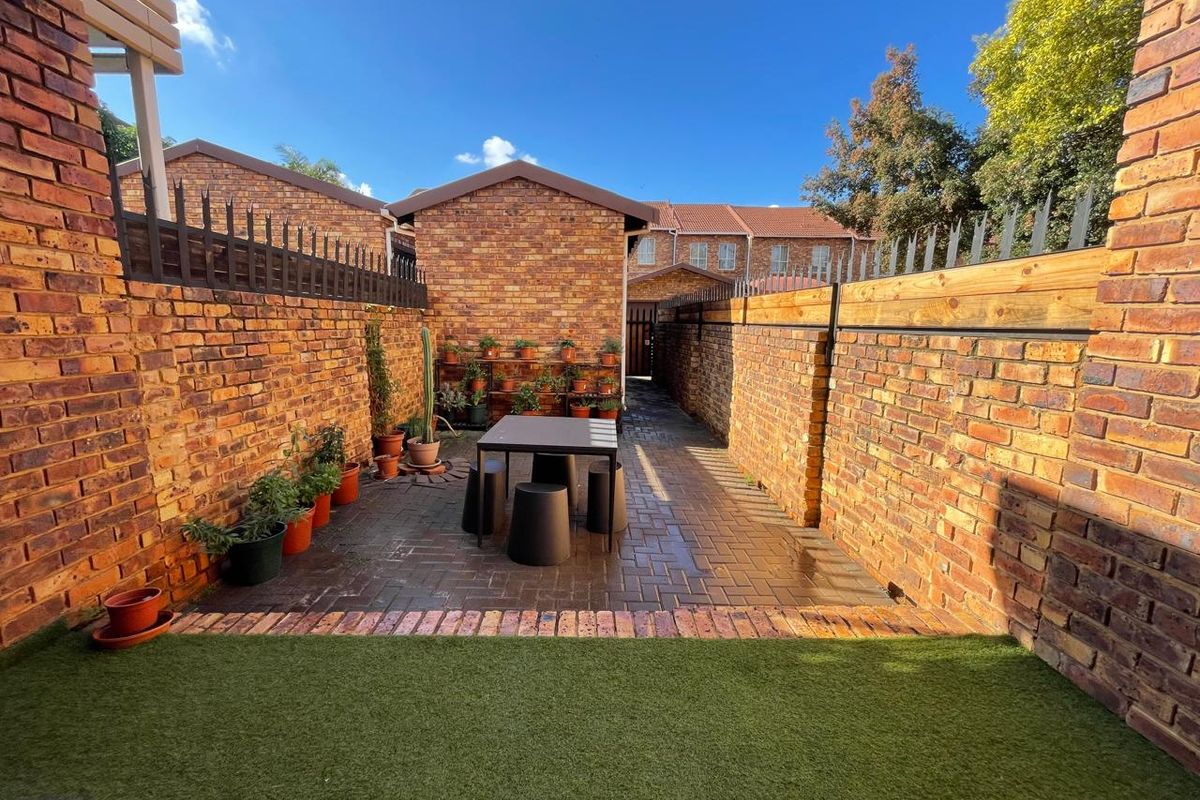 A private rear courtyard featuring brick paving, perimeter brick walls with security spikes, and a section of artificial lawn.