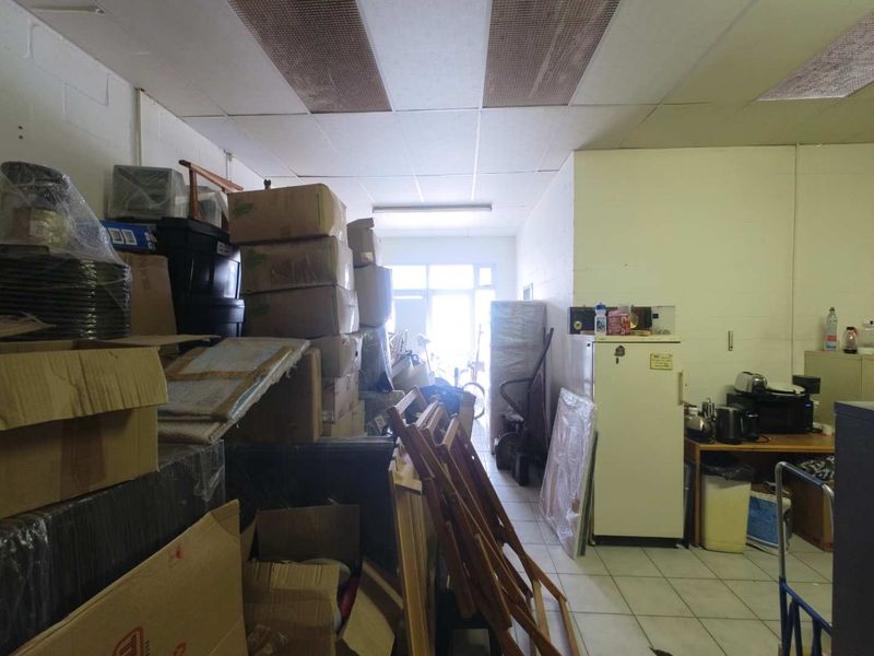 A functional utility or storage space featuring tiled flooring and a suspended ceiling with integrated lighting, currently used for storage.