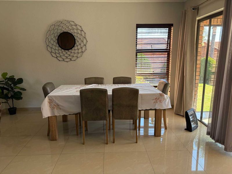 A bright dining area featuring large format floor tiles, a sliding glass door providing garden access, and fitted venetian blinds.