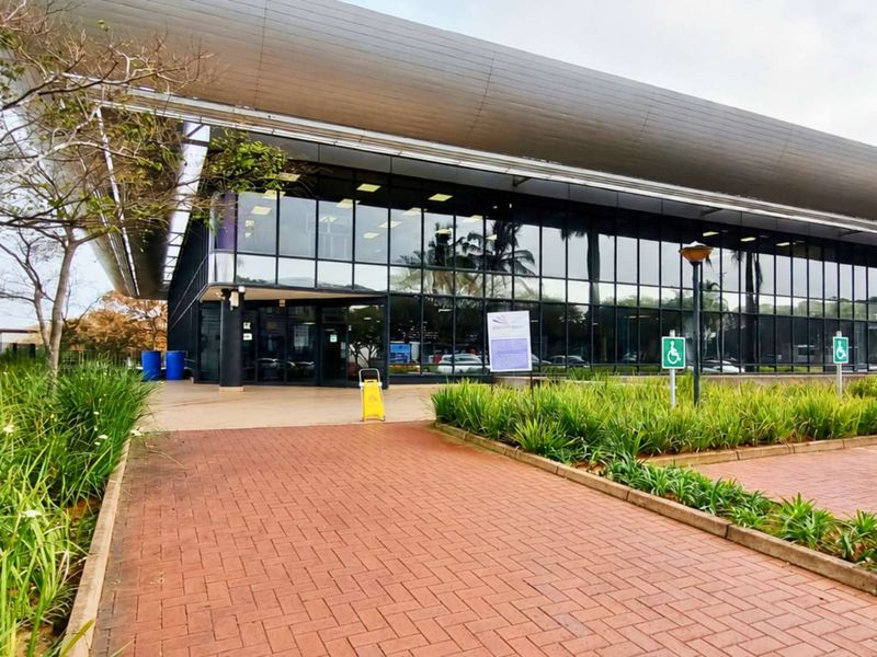 Modern office building exterior featuring extensive glass curtain walling, a prominent metal roof canopy, and paved access with designated accessible parking.