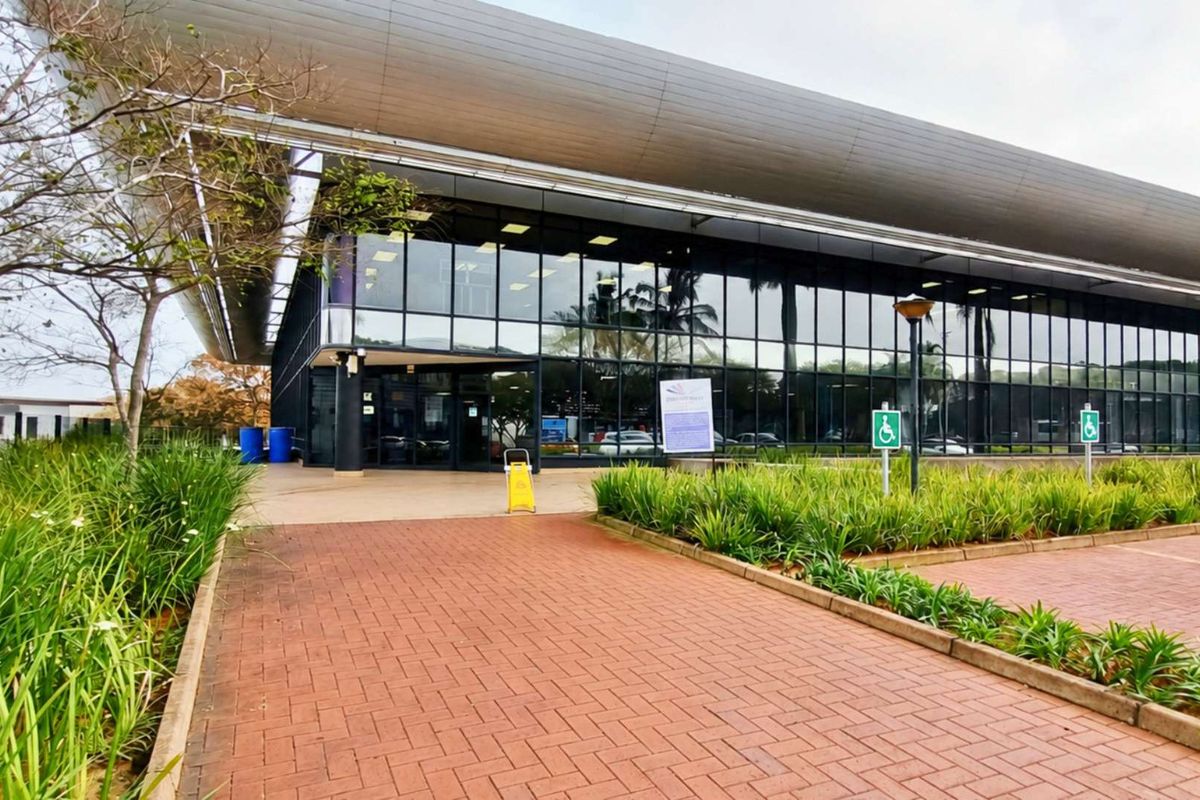 Modern office building exterior featuring extensive glass curtain walling, a prominent metal roof canopy, and paved access with designated accessible parking.
