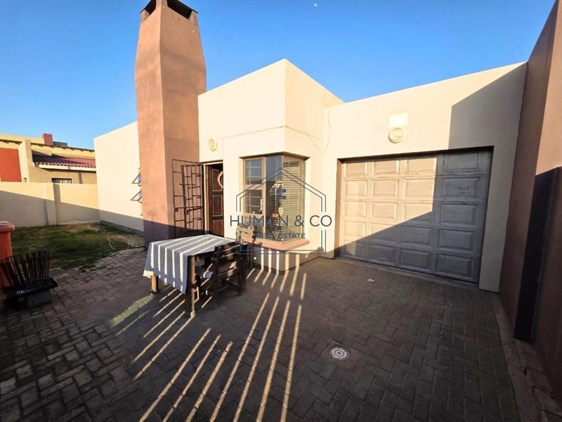 Rear exterior view of the property featuring a brick paved patio area, an external chimney, and a single garage door.