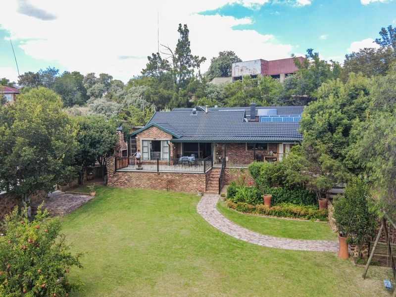 Aerial view of the rear elevation featuring a brick facade, raised patio with metal railing, tiled roof with solar panels, and a landscaped garden.