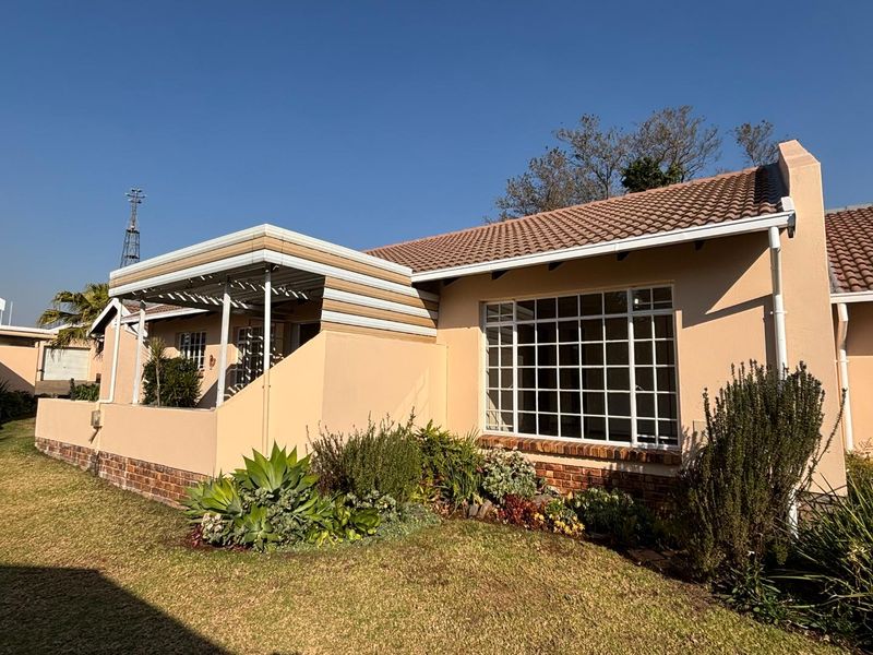 Front elevation of a retirement village unit featuring a tiled roof, brick foundation, and a covered patio area with established garden beds.