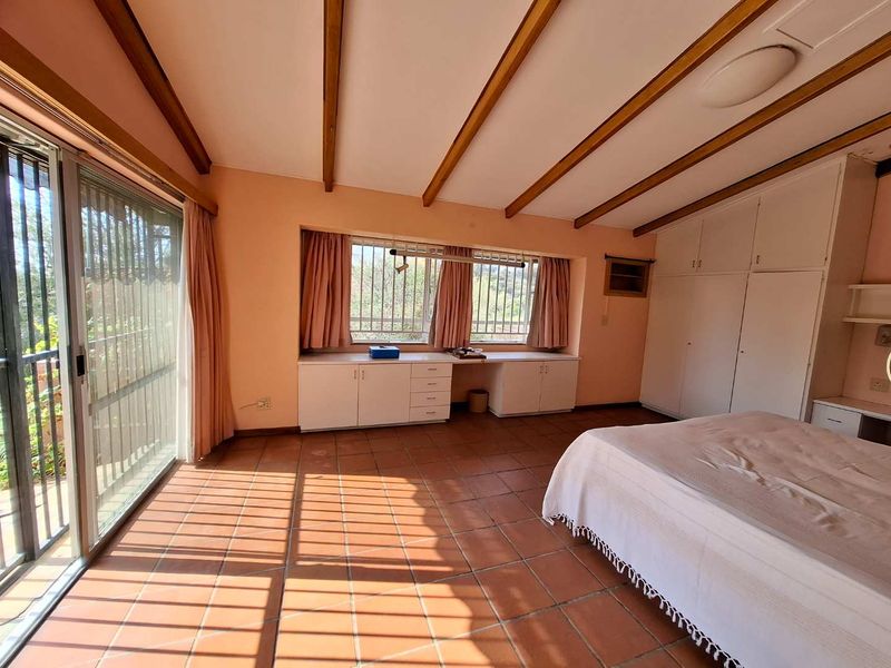 Spacious bedroom featuring terracotta tiled flooring, exposed timber ceiling beams, extensive built-in cabinetry, and large sliding glass doors providing natural light.