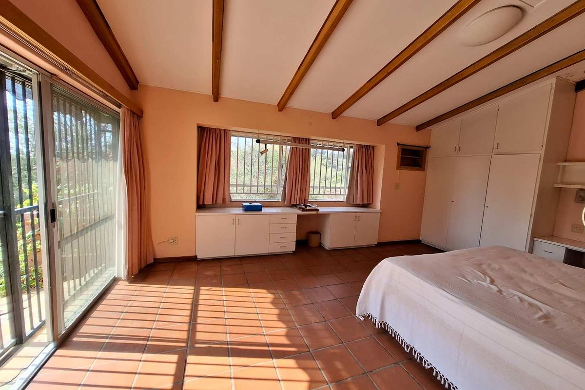 Spacious bedroom featuring terracotta tiled flooring, exposed timber ceiling beams, extensive built-in cabinetry, and large sliding glass doors providing natural light.