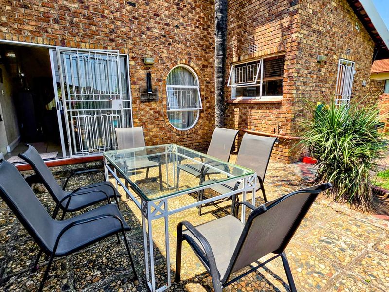 A paved outdoor patio area featuring exposed brick walls, a sliding glass door with security gate, and classic architectural window details.