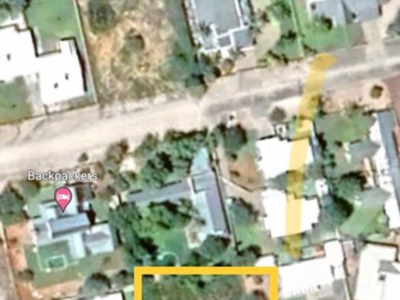 An aerial view showing a vacant residential plot of land highlighted in yellow within a suburban neighborhood.
