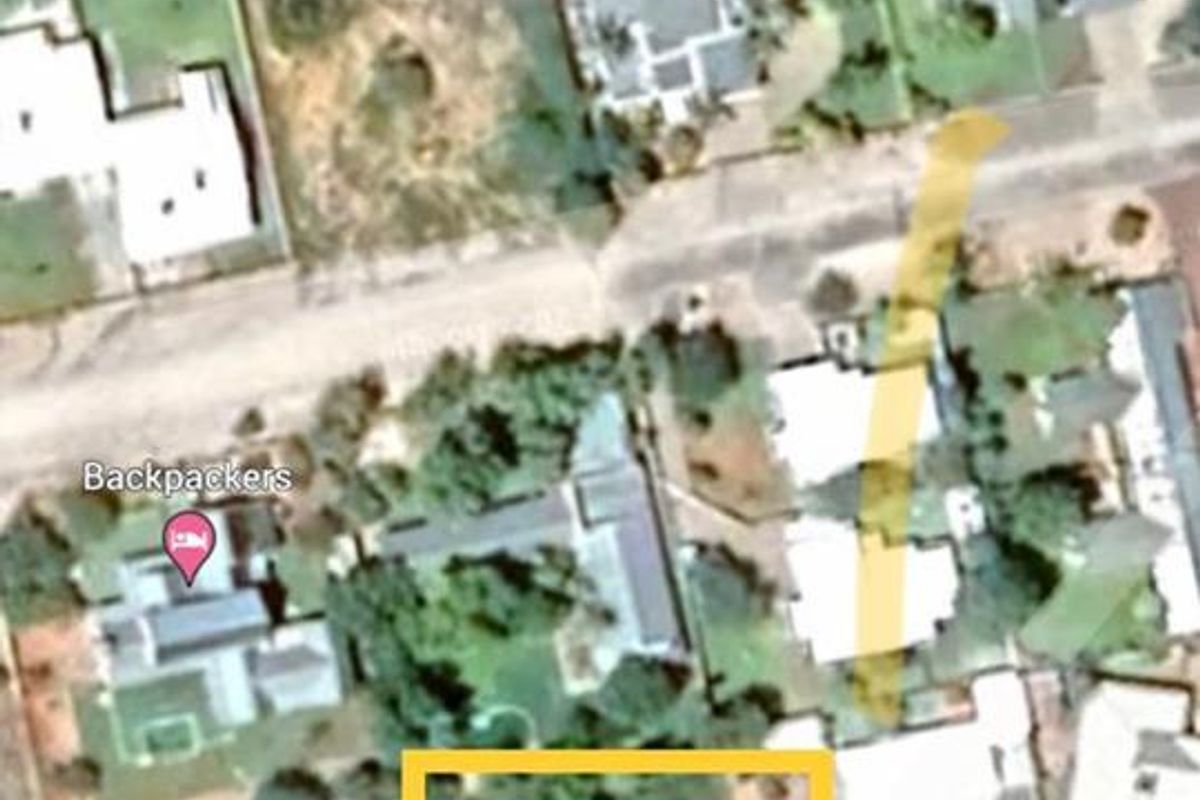 An aerial view showing a vacant residential plot of land highlighted in yellow within a suburban neighborhood.