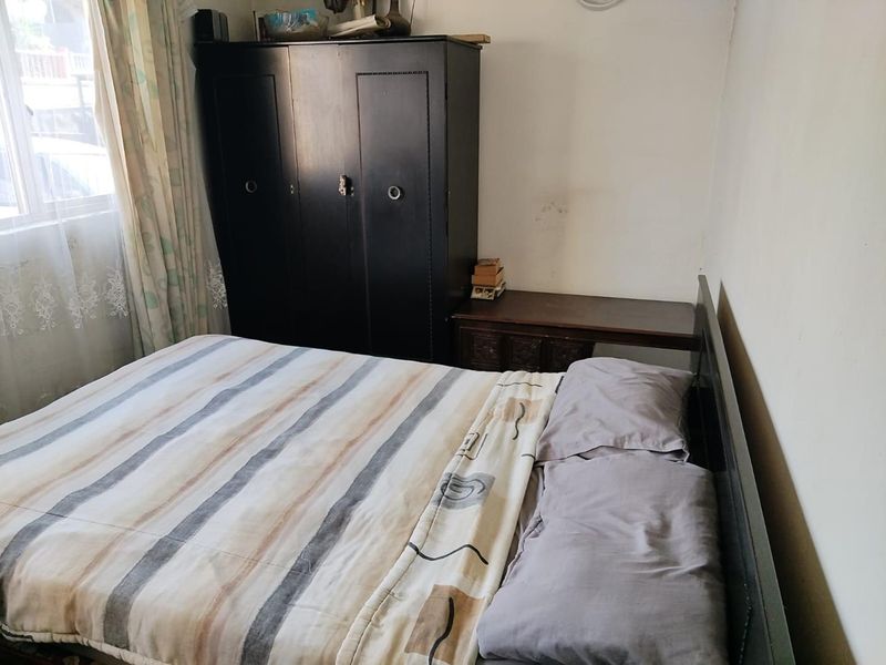 A bedroom featuring a window with curtains and visible wear on the wall surfaces.