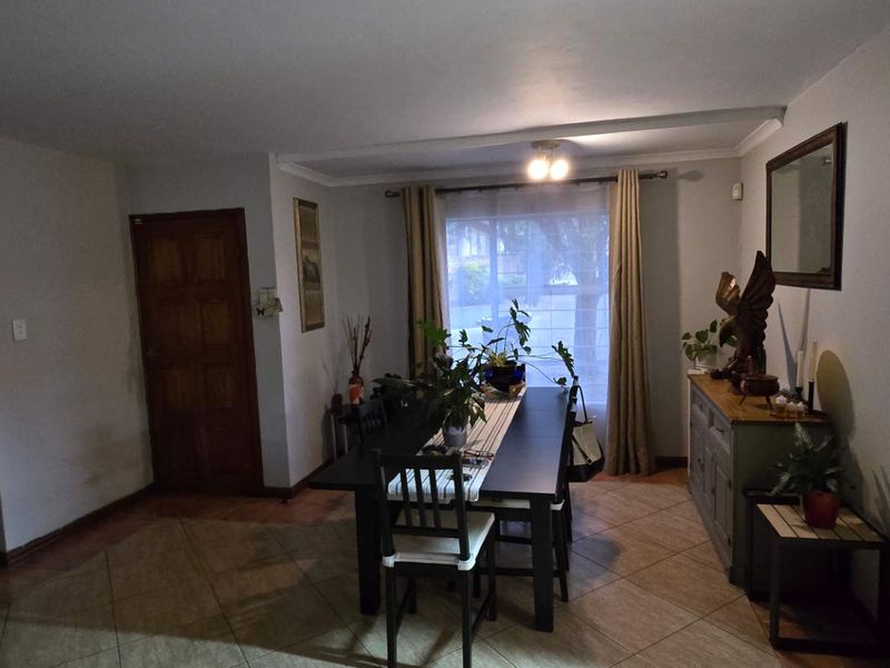 A dining room featuring tiled flooring and wooden doors, providing a functional space for meals with natural light from the window.