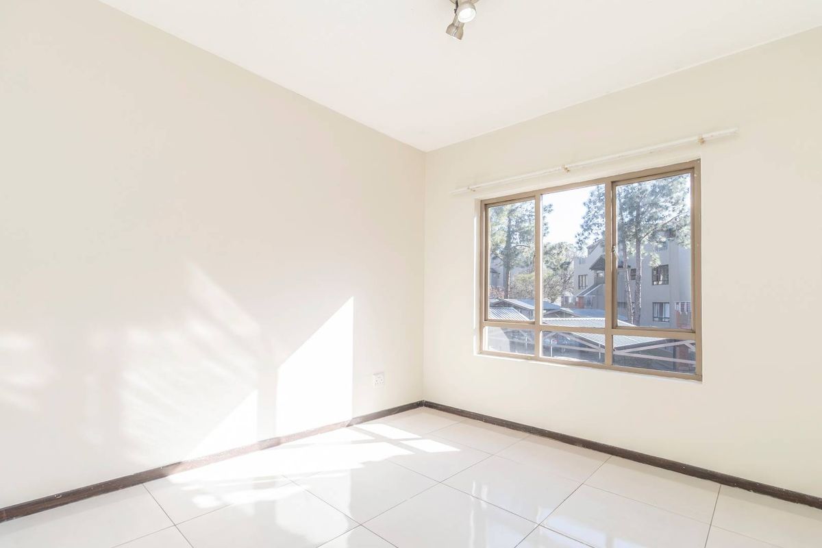 A bright, empty bedroom featuring neutral tiled flooring, large windows with natural light, and a simple ceiling-mounted light fixture.