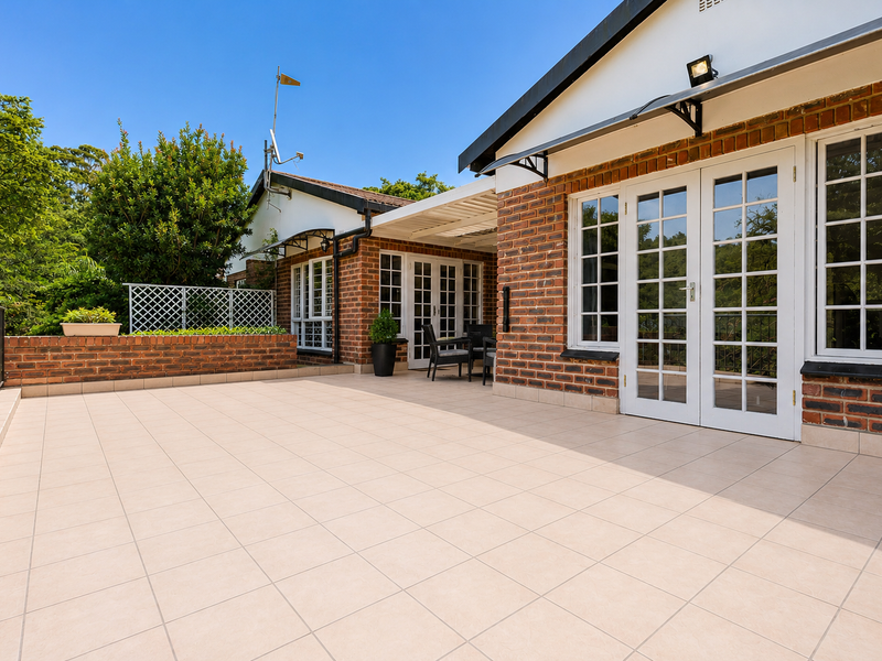 Spacious tiled patio area featuring brick exterior walls, white french doors, and a covered section, ideal for outdoor entertaining.