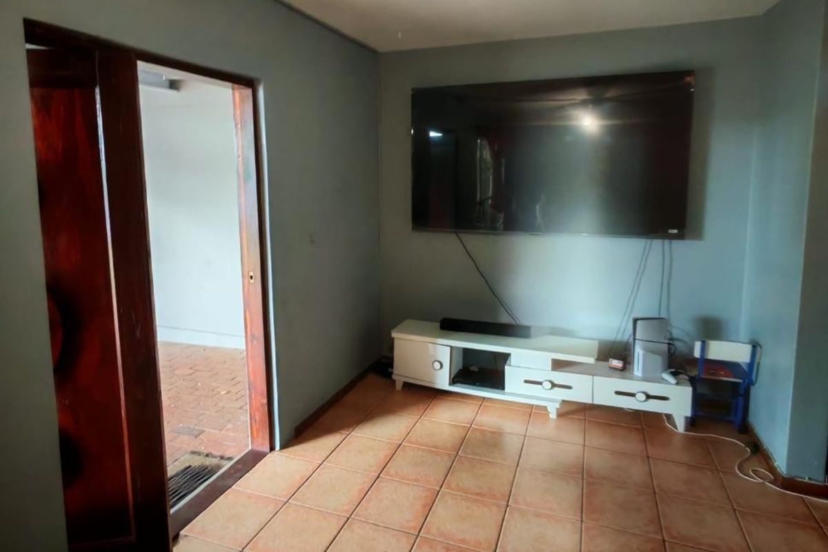 A living room featuring tiled flooring and a ceiling fan, with a wall-mounted television and access to an adjacent outdoor area.
