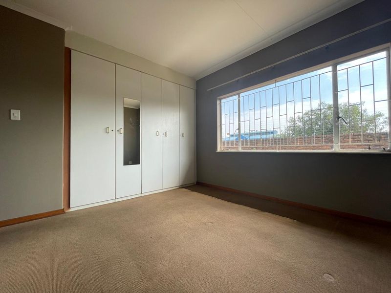 An empty bedroom featuring built-in cupboards, carpet flooring, and a large window with security bars.