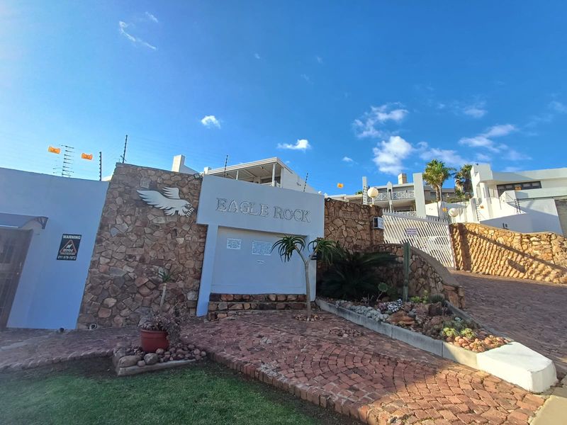 The entrance to Eagle Rock apartment complex featuring stone-clad walls, secure electric fencing, and a paved driveway leading to the residential units.