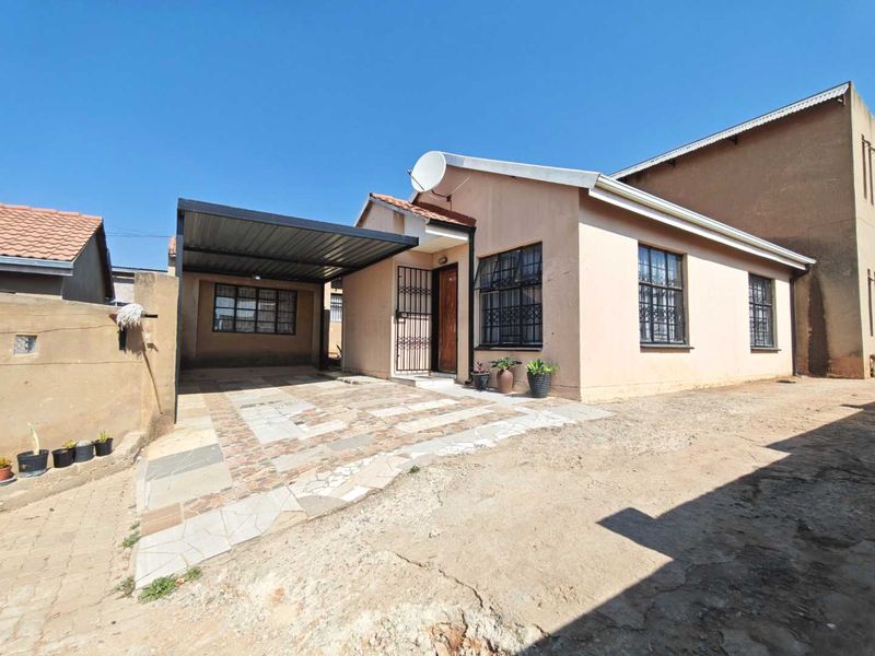 Front elevation of a single-story house featuring a covered carport, security gates, and a tiled driveway area.