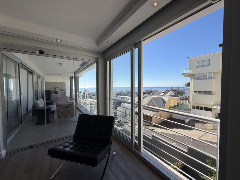Spacious enclosed balcony featuring large sliding glass doors, modern tiled flooring, recessed lighting, and expansive coastal and urban views.