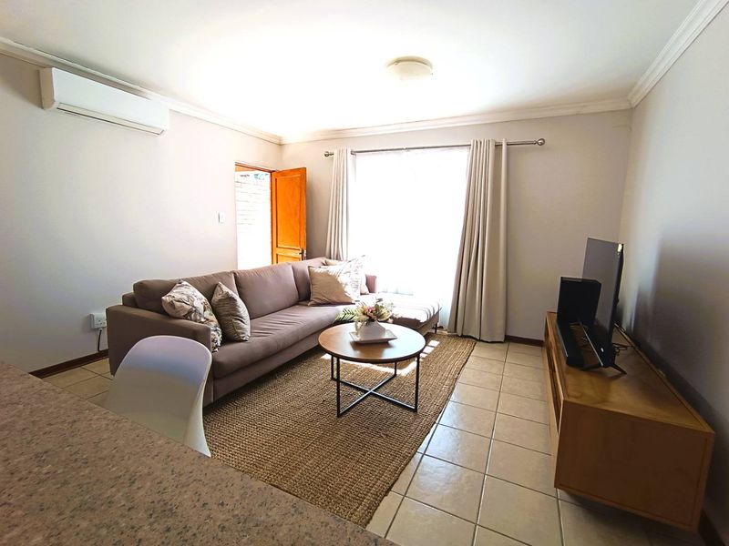 A comfortable living room featuring tiled flooring, a wall-mounted air conditioning unit, and natural light through a large window.