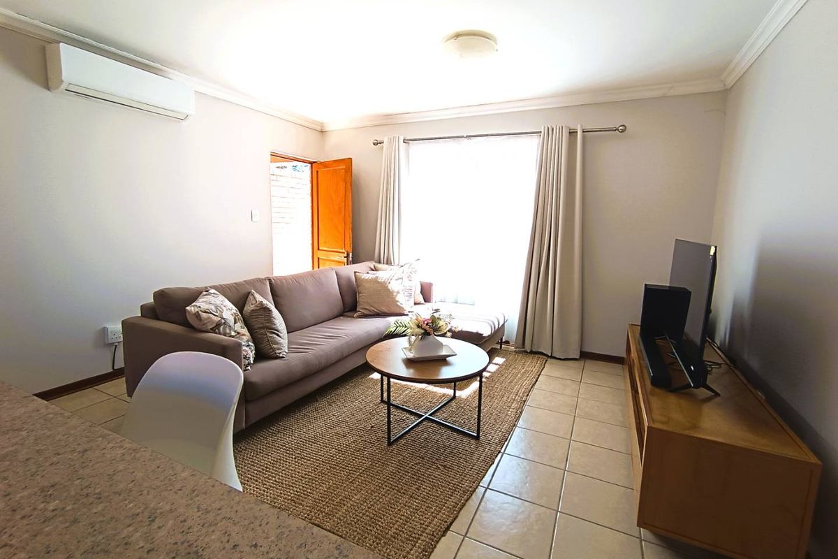 A comfortable living room featuring tiled flooring, a wall-mounted air conditioning unit, and natural light through a large window.