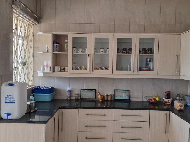 A functional kitchen featuring granite countertops, light wood-finish cabinetry with glass-front upper units, and full-height wall tiling.