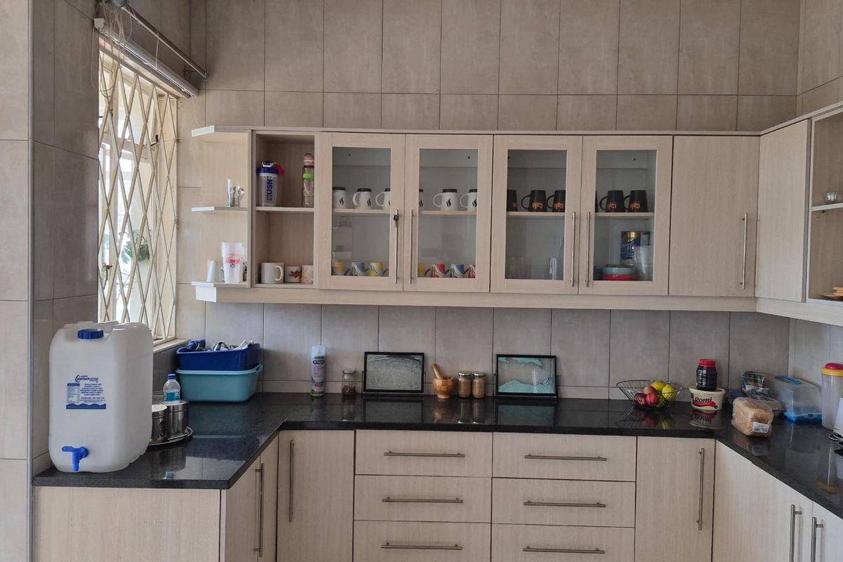 A functional kitchen featuring granite countertops, light wood-finish cabinetry with glass-front upper units, and full-height wall tiling.