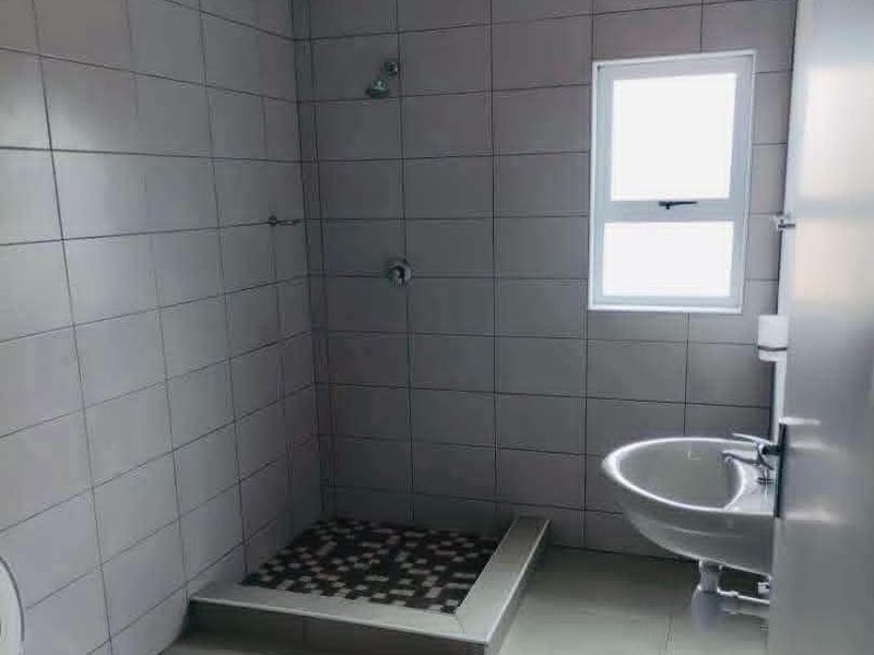 A clean, modern bathroom featuring a walk-in shower with mosaic floor tiling, a wall-mounted basin, and neutral wall tiles throughout.