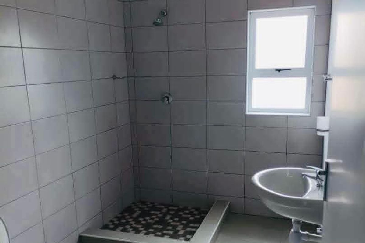 A clean, modern bathroom featuring a walk-in shower with mosaic floor tiling, a wall-mounted basin, and neutral wall tiles throughout.