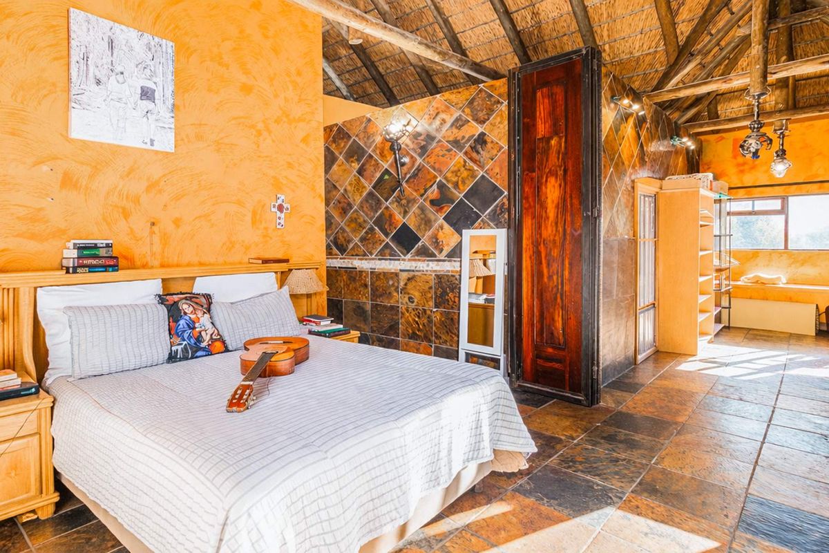 Spacious bedroom featuring a high thatched roof, exposed timber beams, and rustic slate tile flooring with warm-toned textured walls.