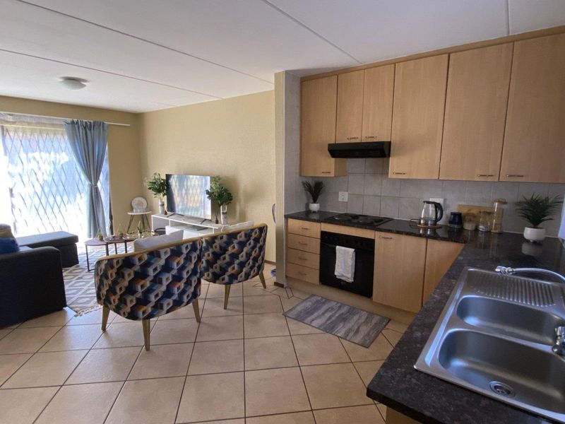 Open-plan living area featuring a functional kitchen with built-in cabinetry, oven, hob, and tiled flooring, flowing into a bright lounge with sliding door access.