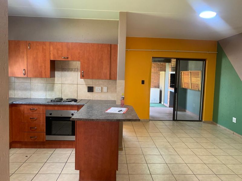 Open plan kitchen and living area featuring wood-finish cabinetry, granite countertops, built-in oven, and tiled flooring with direct access to an outdoor patio.
