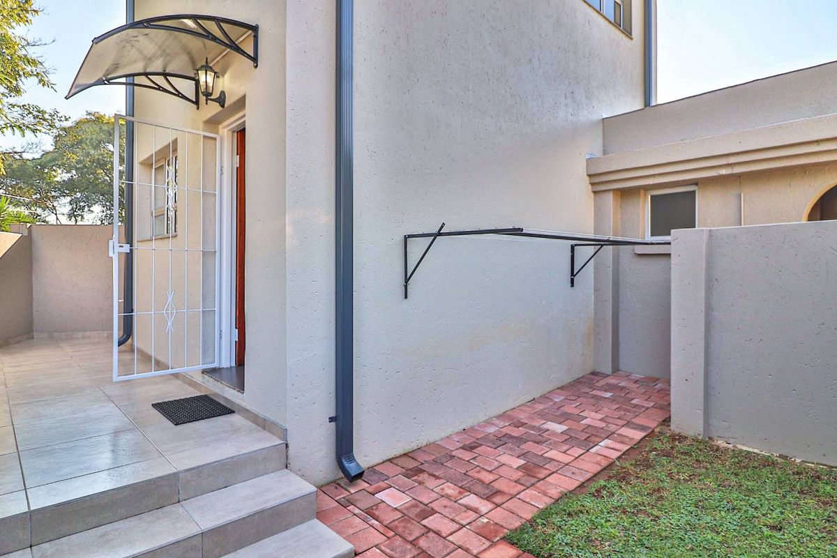 A side exterior view featuring a paved walkway, a security gate with a canopy, and a wall-mounted drying rack.