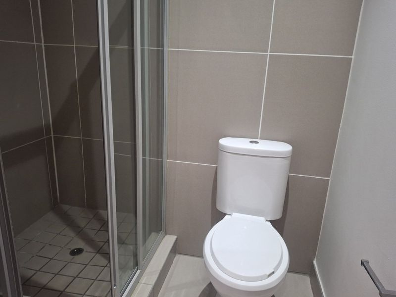 A clean and functional bathroom featuring a glass-enclosed shower, modern toilet, and neutral wall tiling.