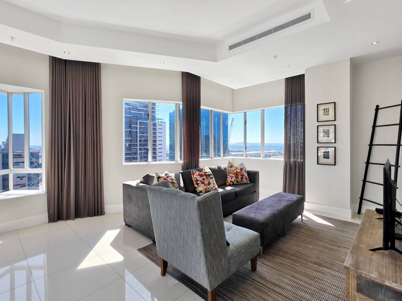 Bright and modern living room featuring large corner windows with city and sea views, tiled flooring, and integrated ducted air conditioning.