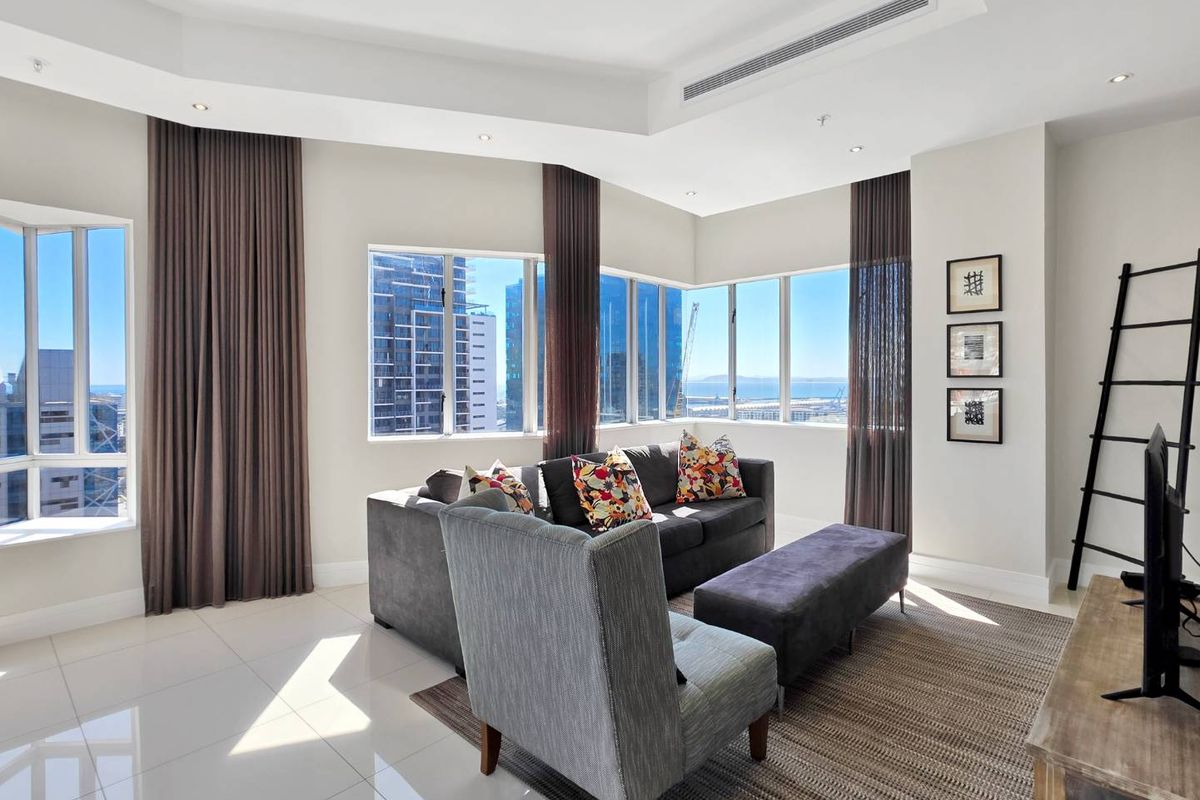 Bright and modern living room featuring large corner windows with city and sea views, tiled flooring, and integrated ducted air conditioning.