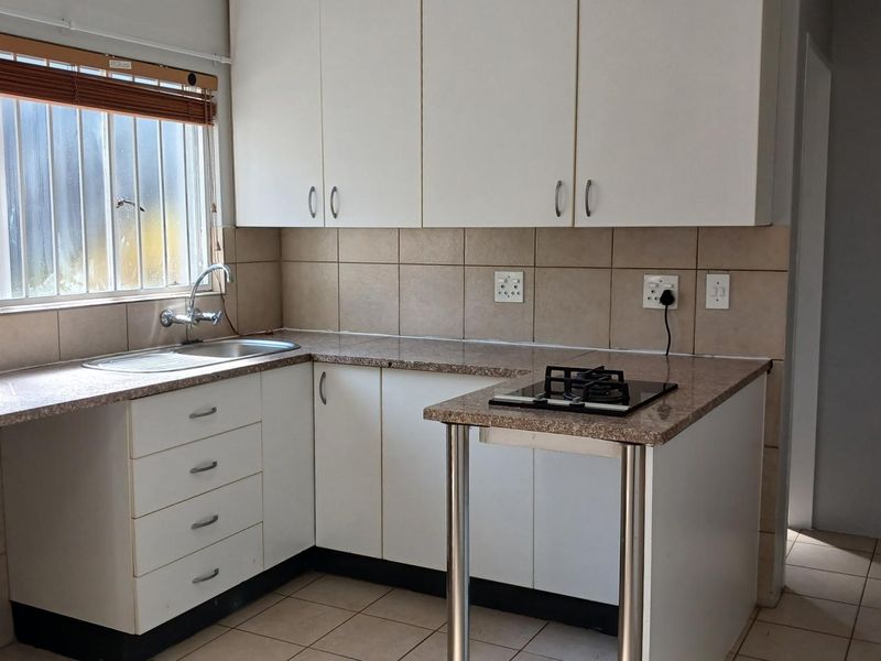 A functional kitchen featuring white cabinetry, laminate countertops, a built-in gas hob, tiled splashbacks, and a stainless steel sink with a window view.