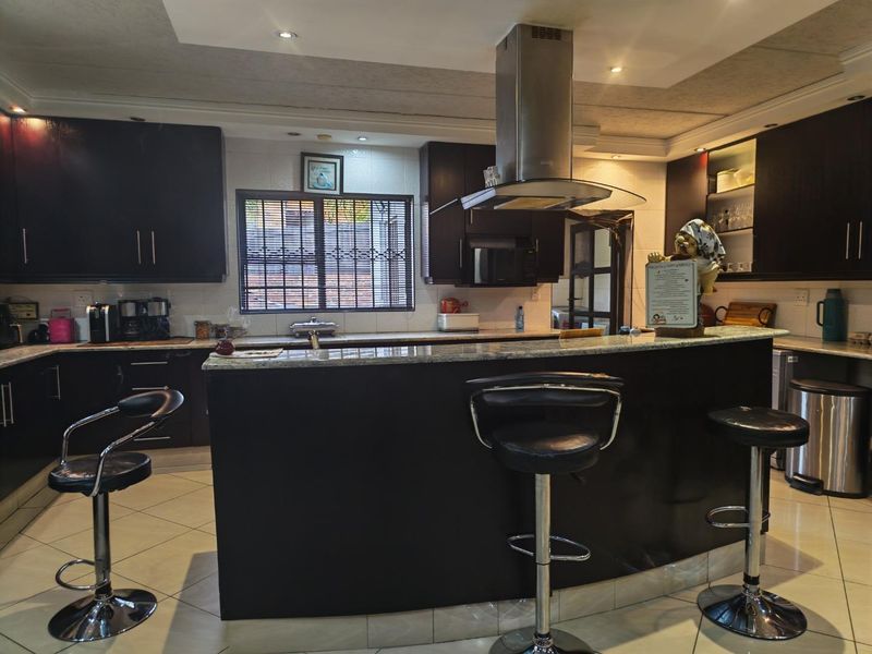 A well-maintained kitchen featuring dark wood cabinetry, granite countertops, a central breakfast bar, and a stainless steel extractor fan.