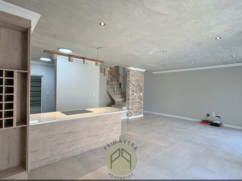 Spacious open-plan living area featuring a modern kitchen island, built-in wine storage, and a striking exposed brick pillar with an adjacent staircase.