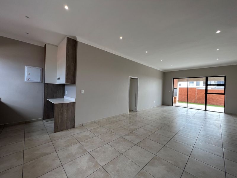 Spacious open-plan living area featuring neutral tiled flooring, recessed downlighting, and a sliding glass door providing access to the rear patio.