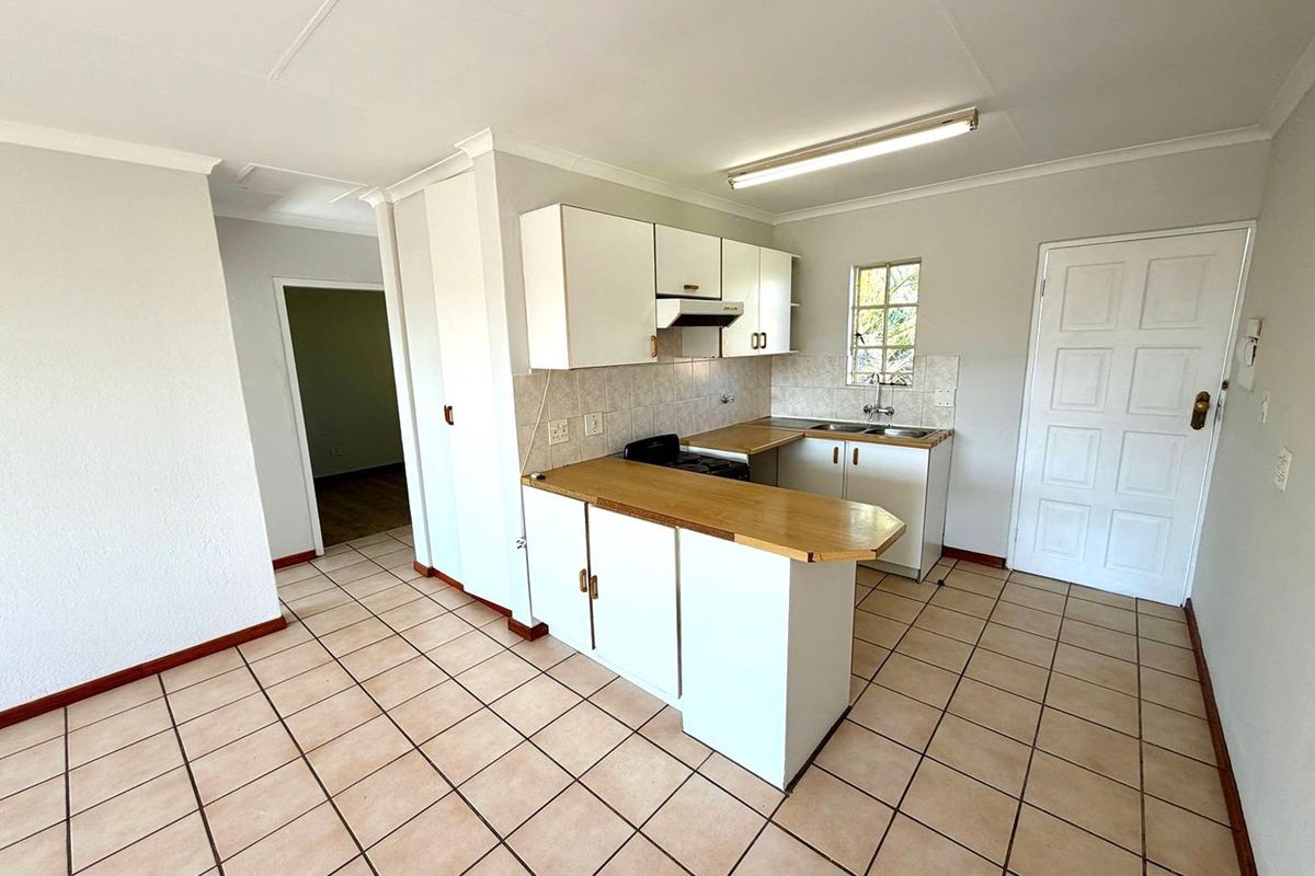 A functional kitchen featuring white cabinetry, wooden countertops, a built-in stove with extractor fan, and tiled flooring in an open-plan layout.