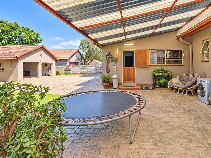 A spacious covered patio area with paved flooring, featuring a stable door entrance and views of the paved driveway and detached garage.