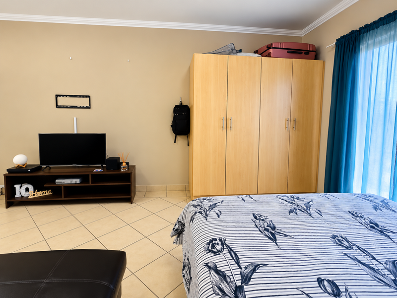 A bedroom featuring tiled flooring, a built-in wooden wardrobe, and neutral wall tones, providing a functional space with natural light access.