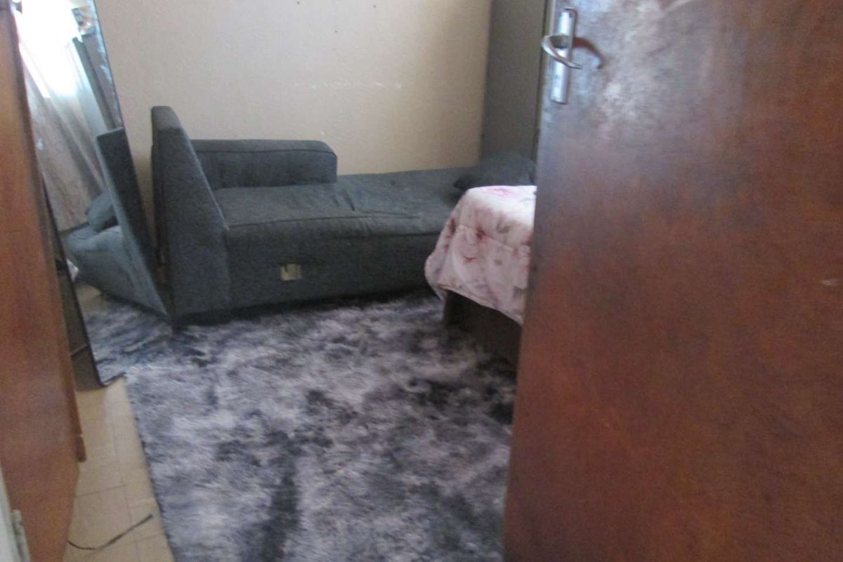 A bedroom interior featuring tiled flooring and a standard door entrance, showing signs of wear and requiring cosmetic updates.